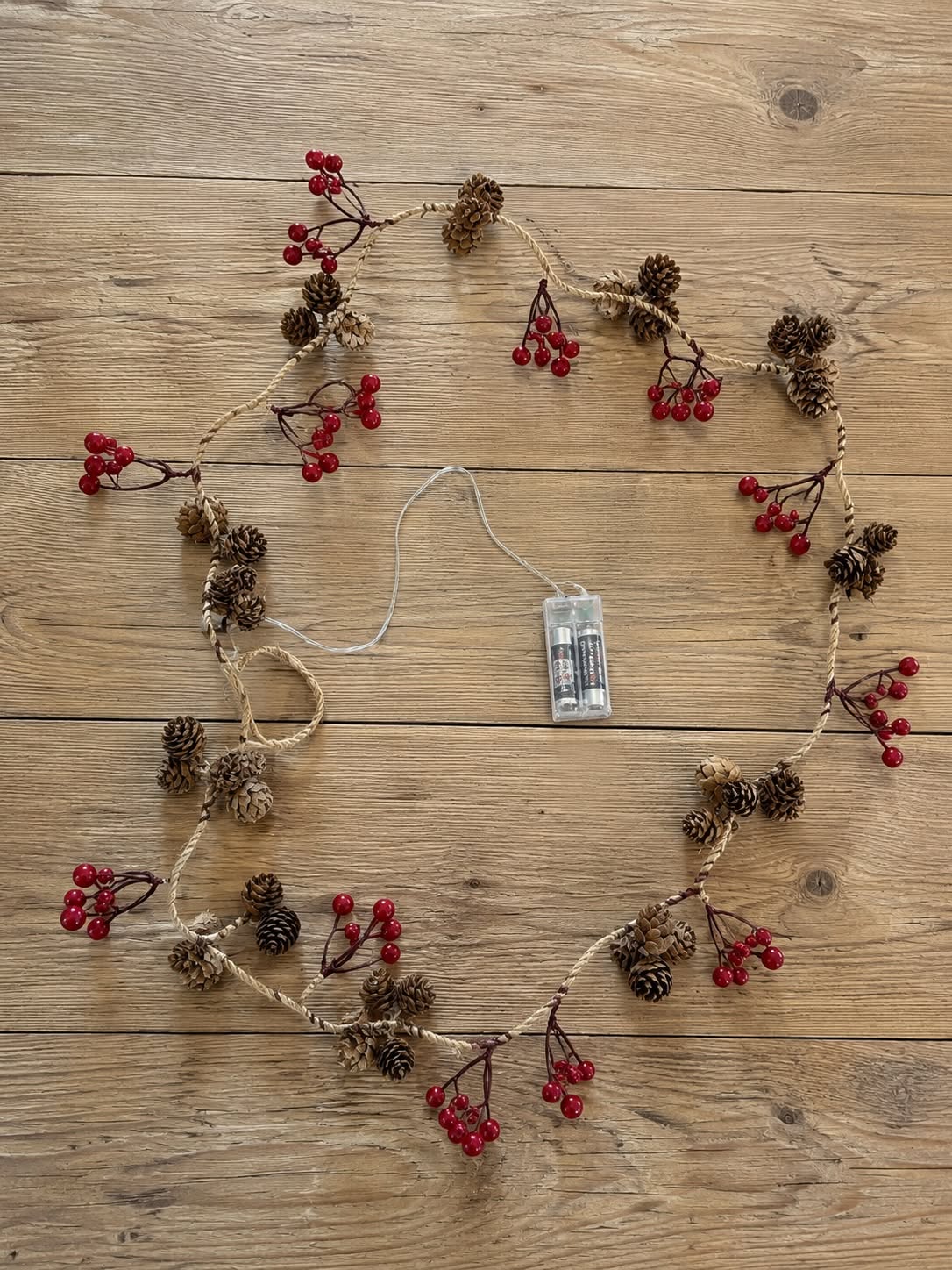 Lichterkette mit roten Beeren und Zapfen